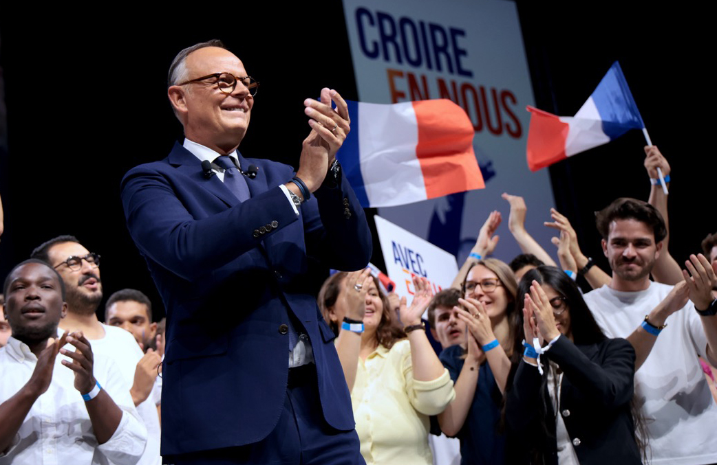 Édouard Philippe applaudit sur scène, entouré de sympathisants et de drapeaux français, devant le slogan « Croire en nous ».